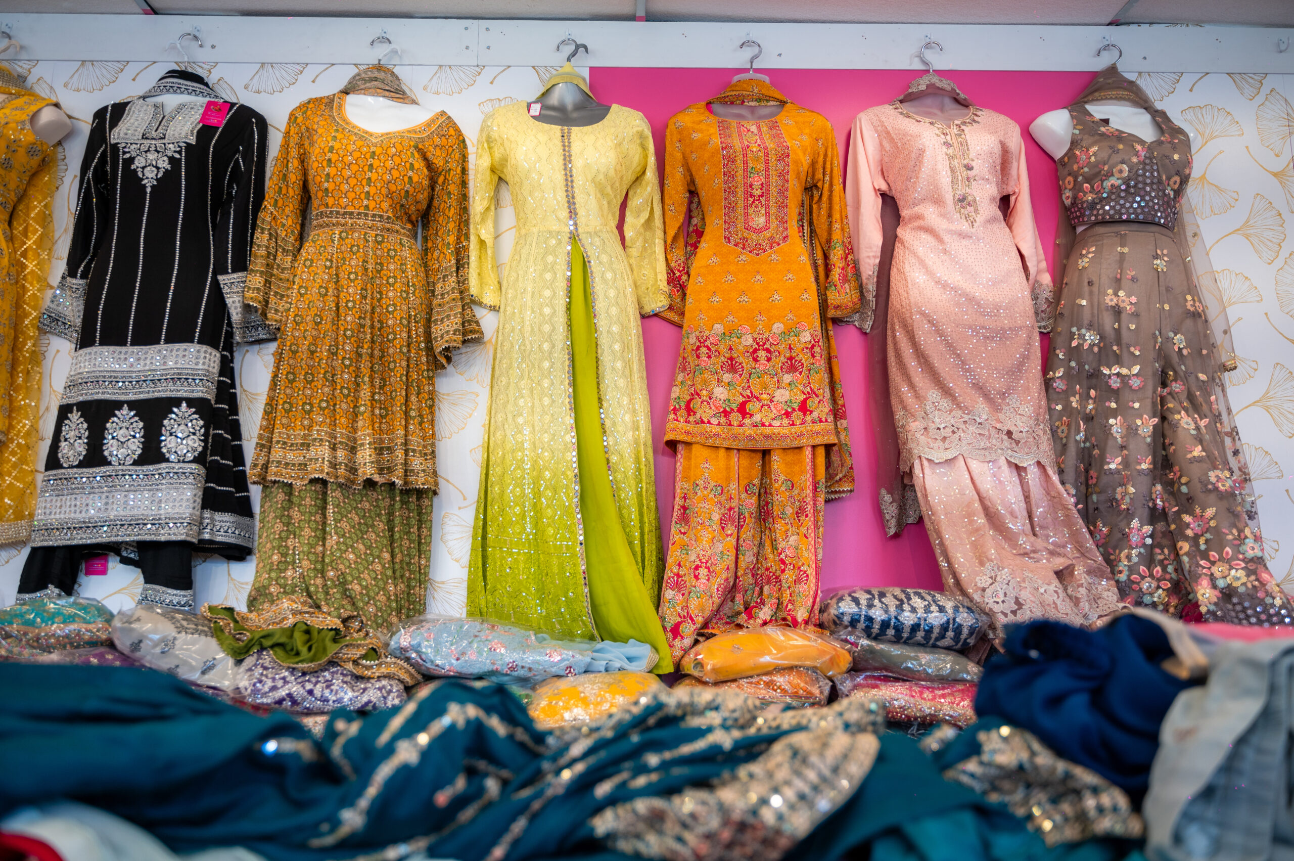 Handmade embroidered tunics and pants in a variety of colours and patterns adorn a wall.